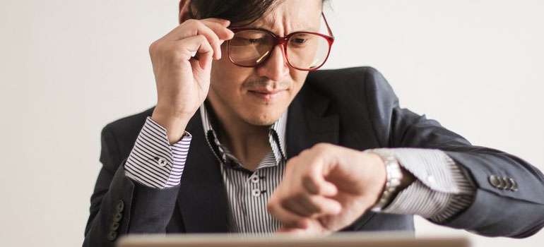 A man in a suit wearing glasses, checking the time on his wristwatch