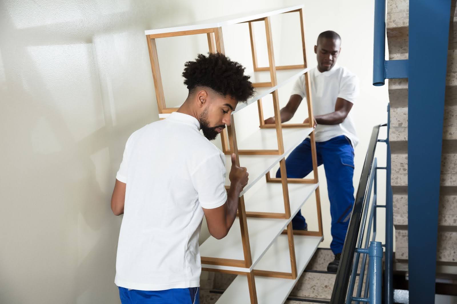 two male movers carrying a shelf up stairs